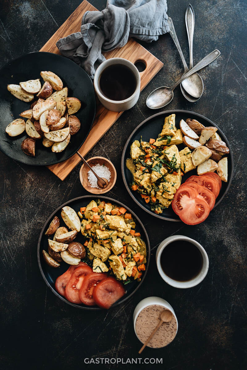 Curry tofu scramble on plates with roasted potatoes and tomatoes