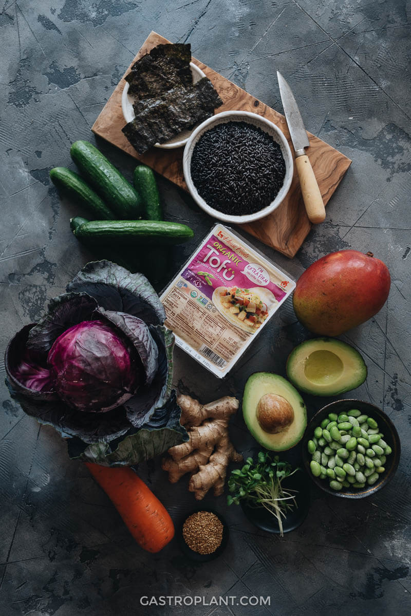 Raw fresh ingredients - cucumber, House Foods tofu, avocado, carrot, edamame, mango, and rice - spread on a table