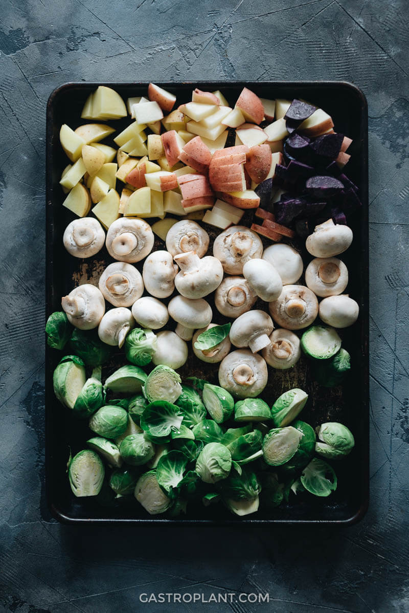 Raw brussels sprouts, potatoes, and mushrooms on a baking tray