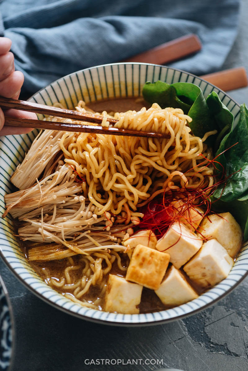 Chopsticks pulling ramen noodles from a hot bowl of vegan Japanese curry broth