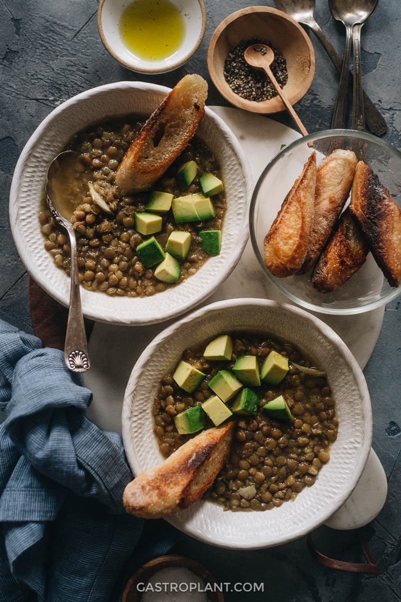 Two bowls of vegan lentil soup with toasted bread and avocado cubes