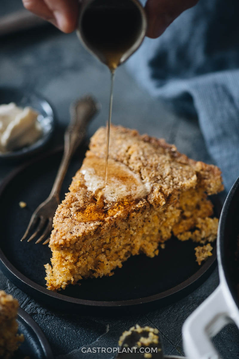 A slice of vegan cornbread with maple syrup drizzled on it