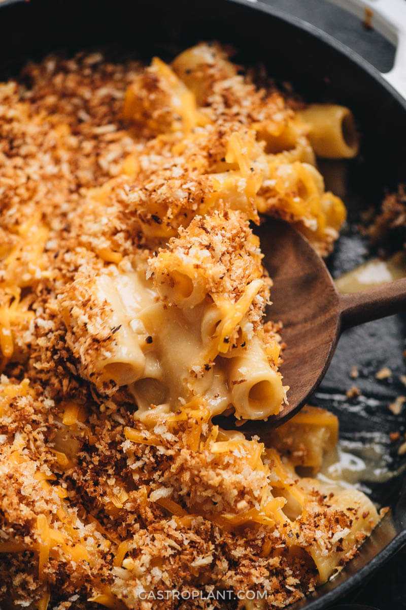 Cheesy vegan noodles topped with breadcrumbs being scooped with a wooden spoon