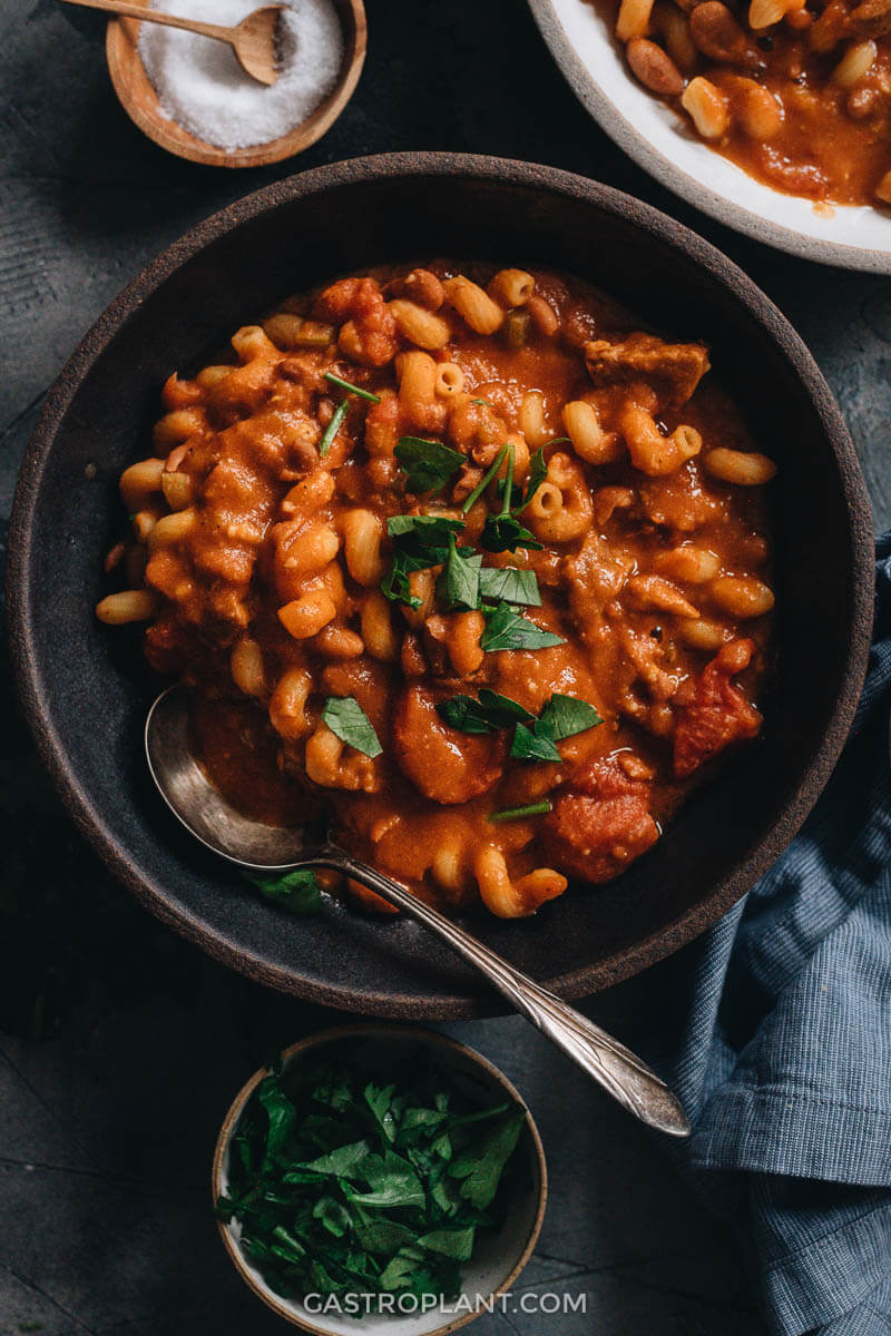 A black bowl of hearty vegan pasta, bean, and tomato soup