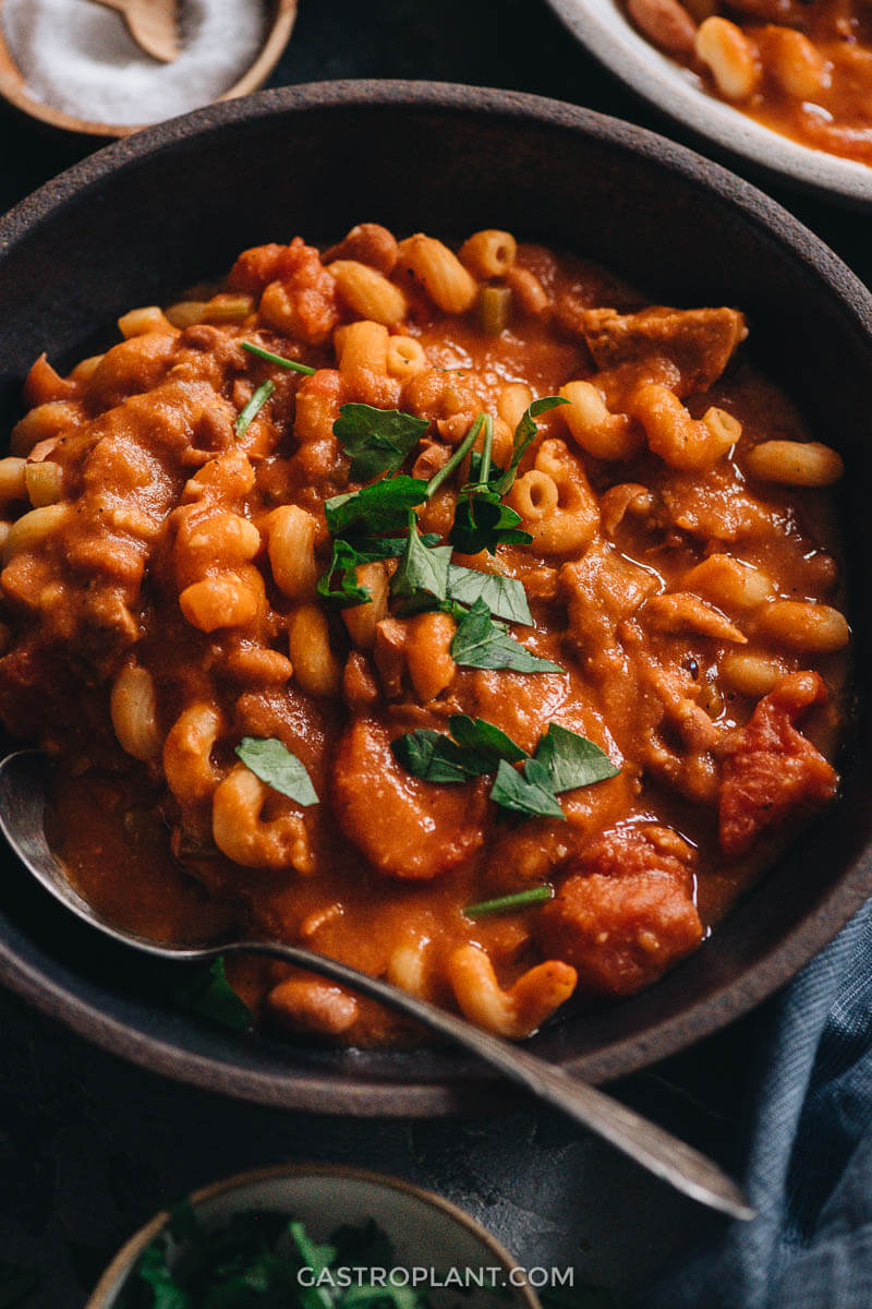 Close-up photo of vegan pasta bean soup with tomato and vegan sausage topped with parsley