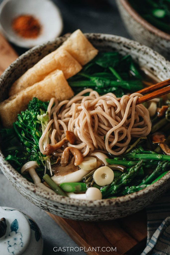 Pulling soba soba buckwheat noodles from a bowl of vegan soup with chopsticks