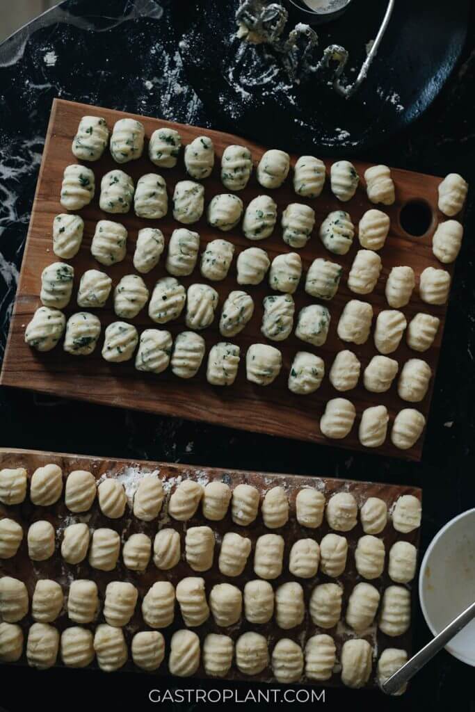 Two cutting boards filled with uncooked vegan gnocchi, some with herbs and some without