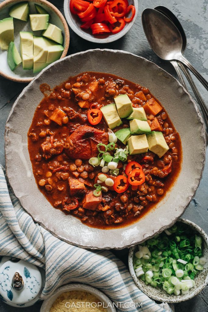 A bowl of bright red vegan chili garnished with avocado and red chile peppers