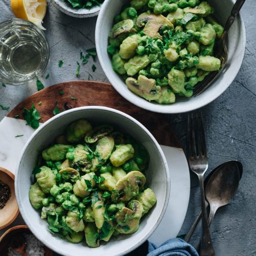 Two bowls of green pea pasta (gnocchi) with peas and mushrooms and lemon