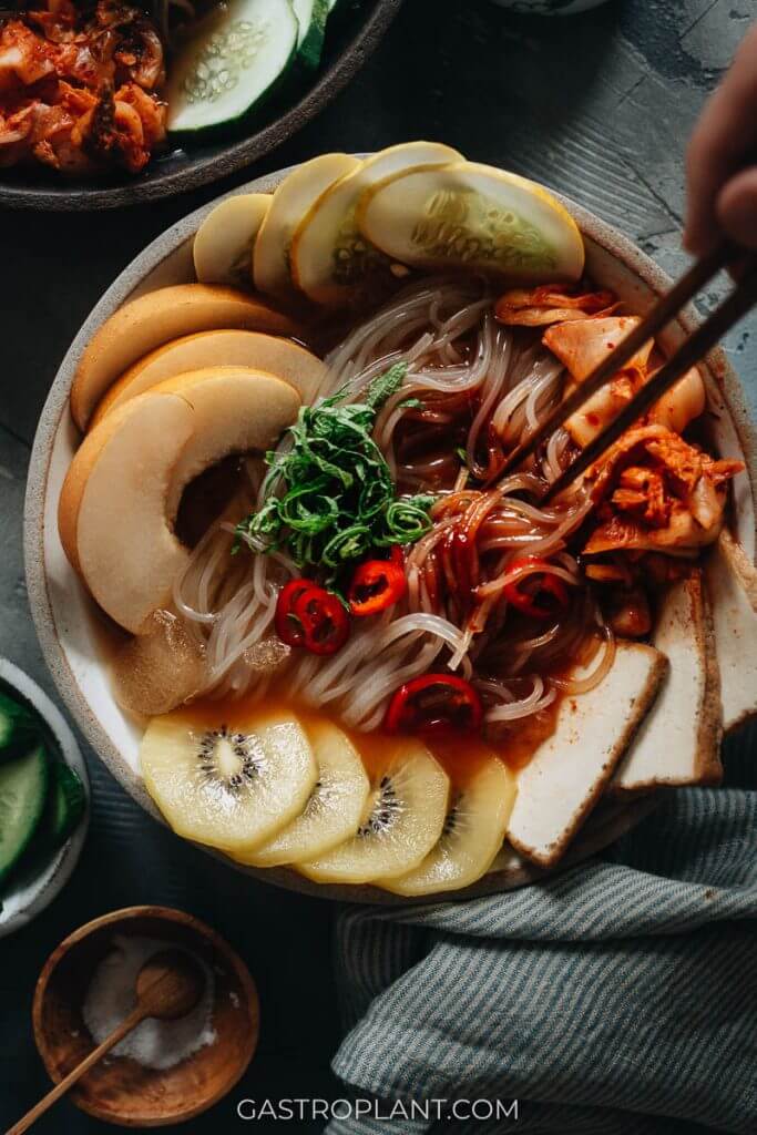 Korean cold noodles (mul naengmyeon) with kiwi, Asian pear, and kimchi in sweet sour spicy broth