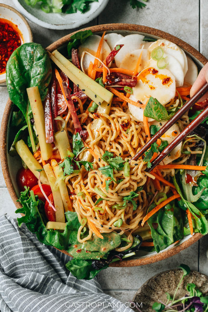 A bowl of Chinese sesame noodles with salad, cucumber, beet, carrot, and radish (vegan)