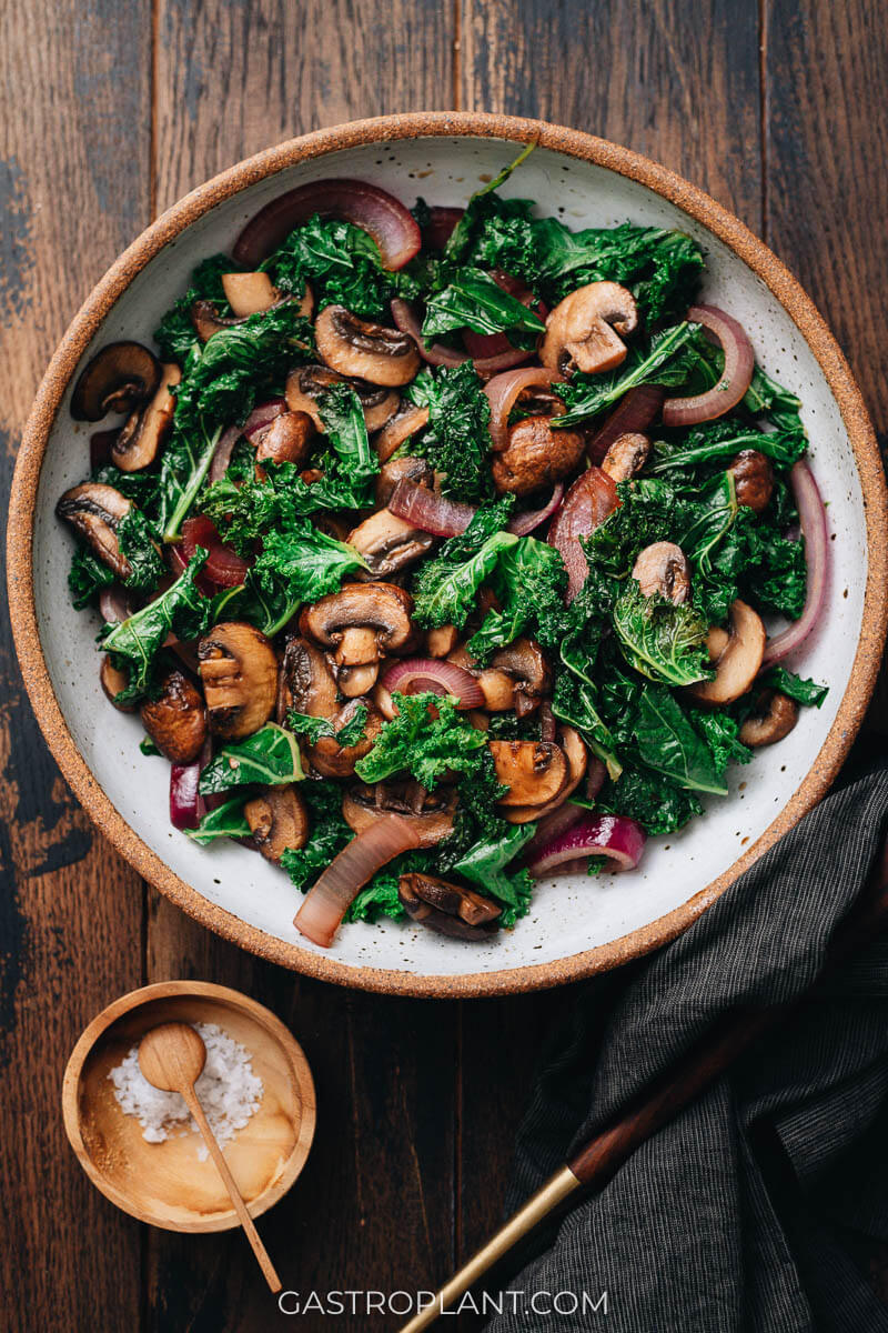 A bowl on a table with kale, mushroom, and red onion