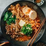 Plant-based ramen in a black bowl with red kimchi broth