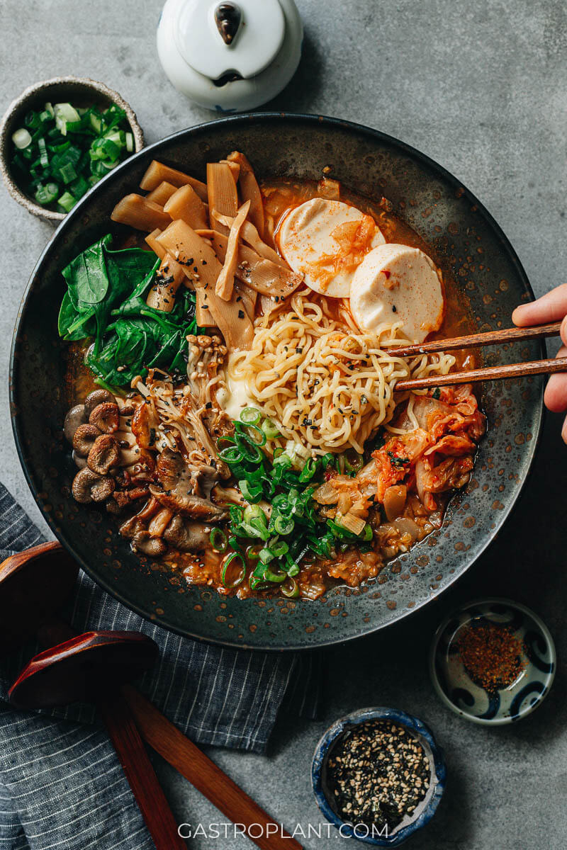 A bowl of spicy ramen noodles with kimchi, tofu, mushrooms, and bamboo