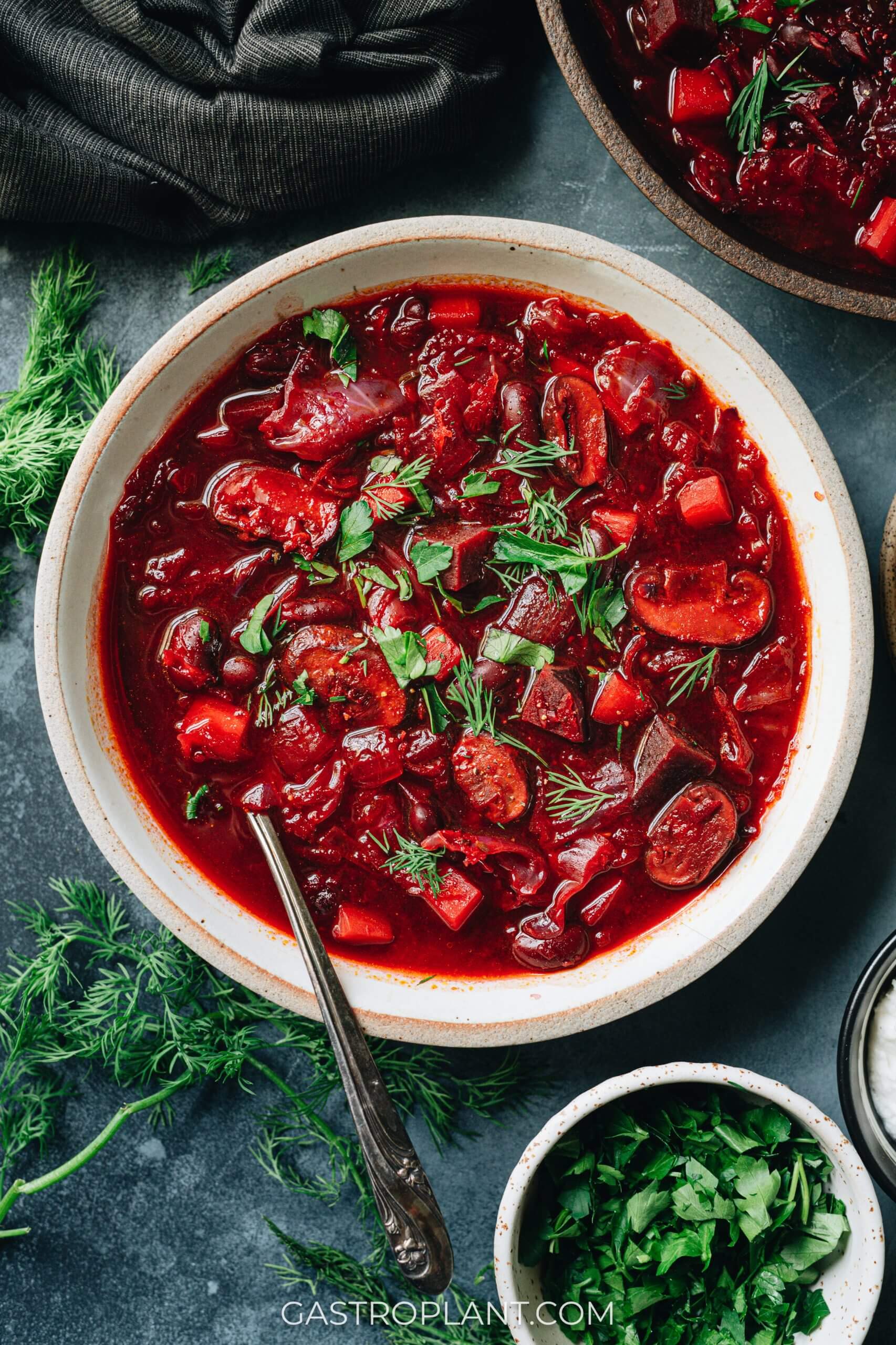 A bowl of striking scarlet borscht, made for rich flavor with vegan ingredients and garnished with dill and parsley