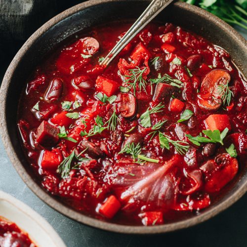 A comforting bowl of vegan red beet soup with cabbage, potato, beans, mushrooms, and more